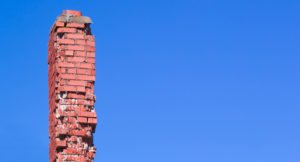 A damaged brick chimney against a blue sky
